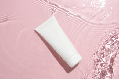 Photo of Cosmetic product. Tube with cream in water on pink background, top view