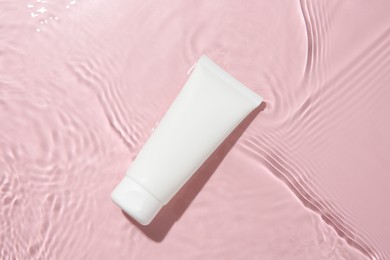 Photo of Cosmetic product. Tube with cream in water on pink background, top view