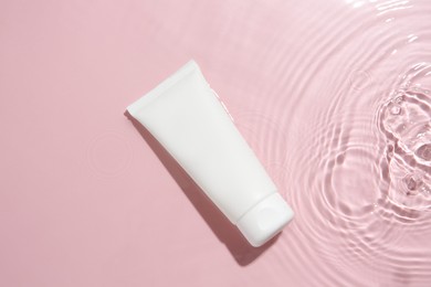 Photo of Cosmetic product. Tube with cream in water on pink background, top view