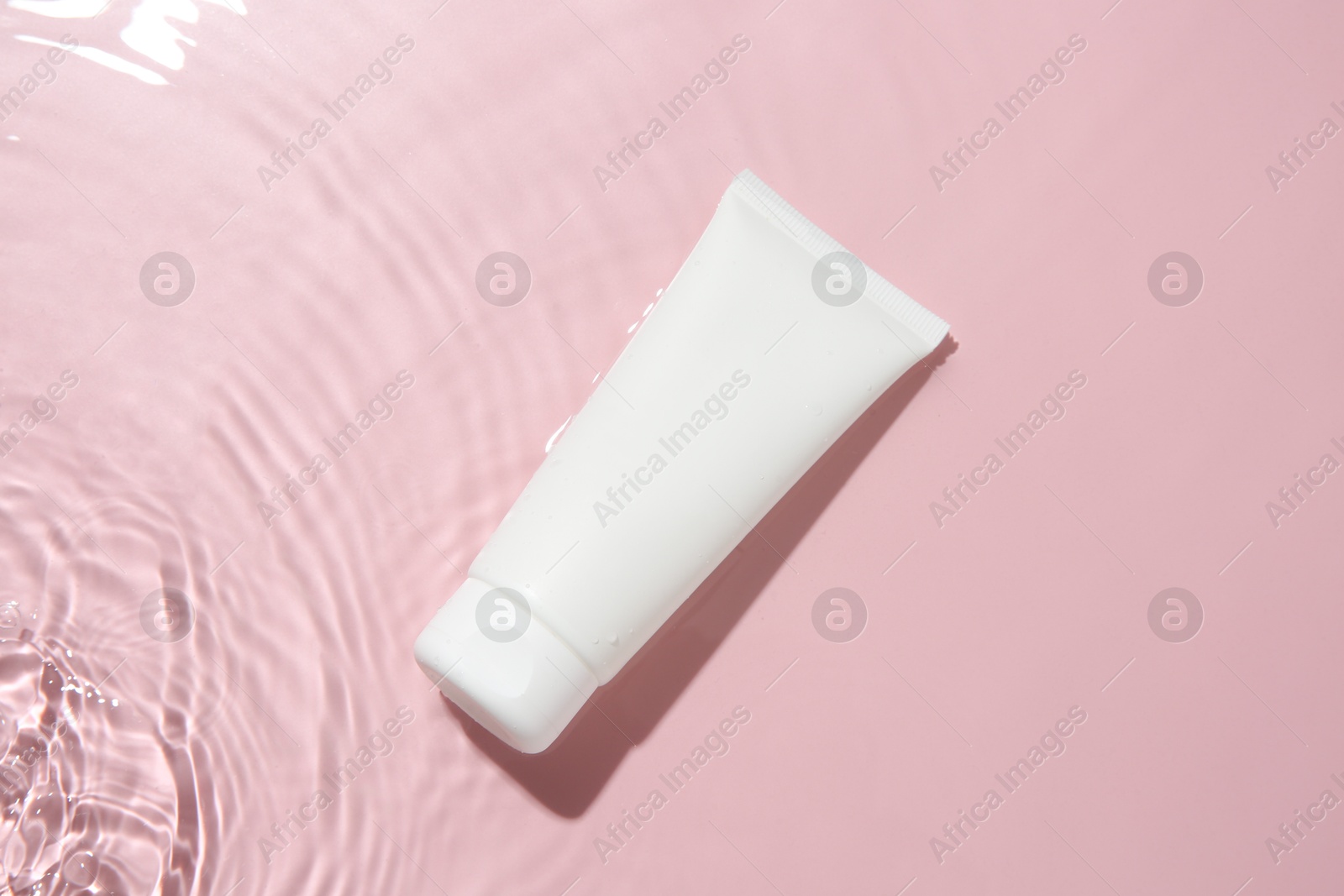 Photo of Cosmetic product. Tube with cream in water on pink background, top view