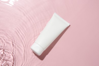 Cosmetic product. Tube with cream in water on pink background, top view