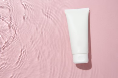 Photo of Cosmetic product. Tube with cream in water on pink background, top view. Space for text