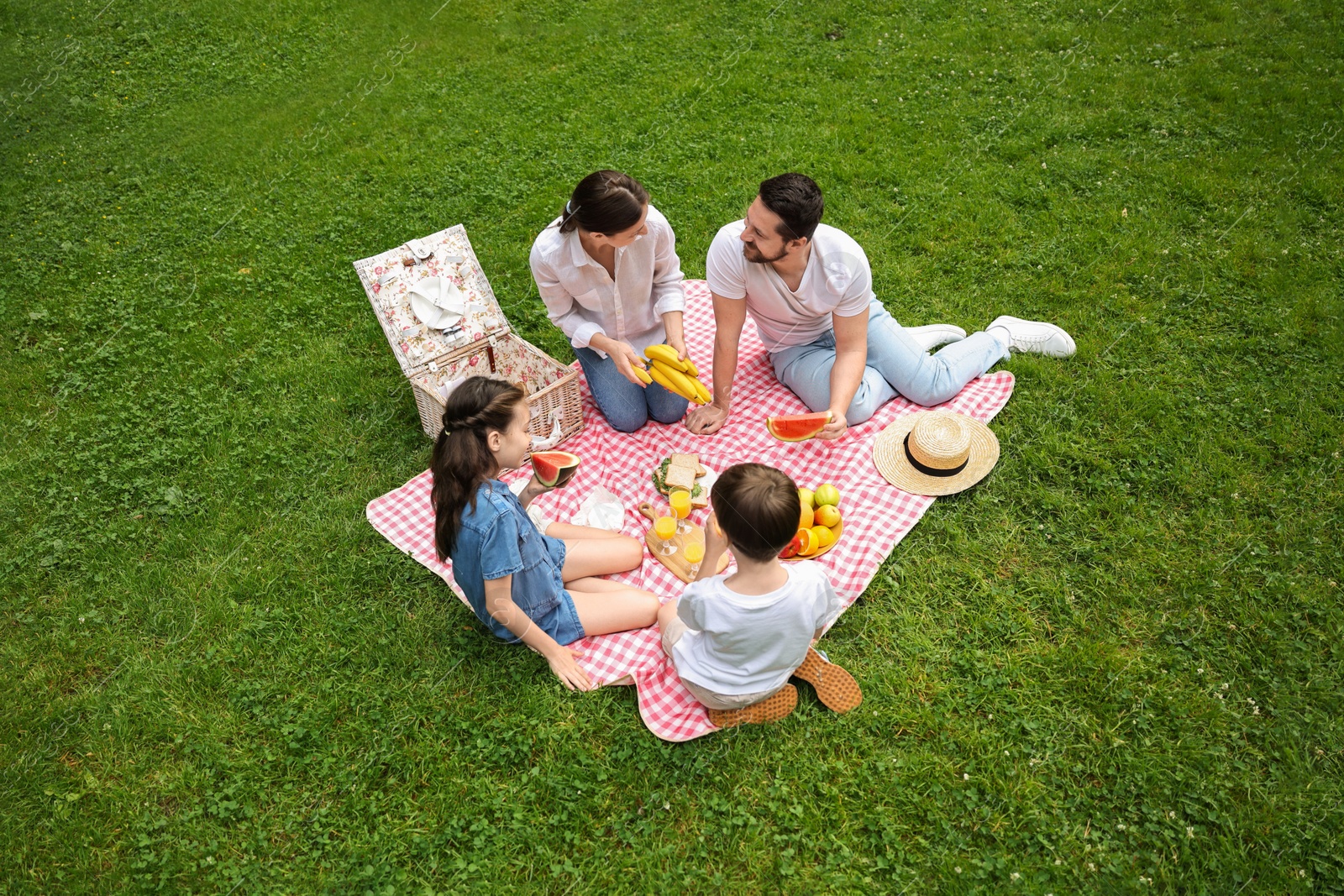 Photo of Family picnic. Parents and their children eating on green grass outdoors, above view. Space for text