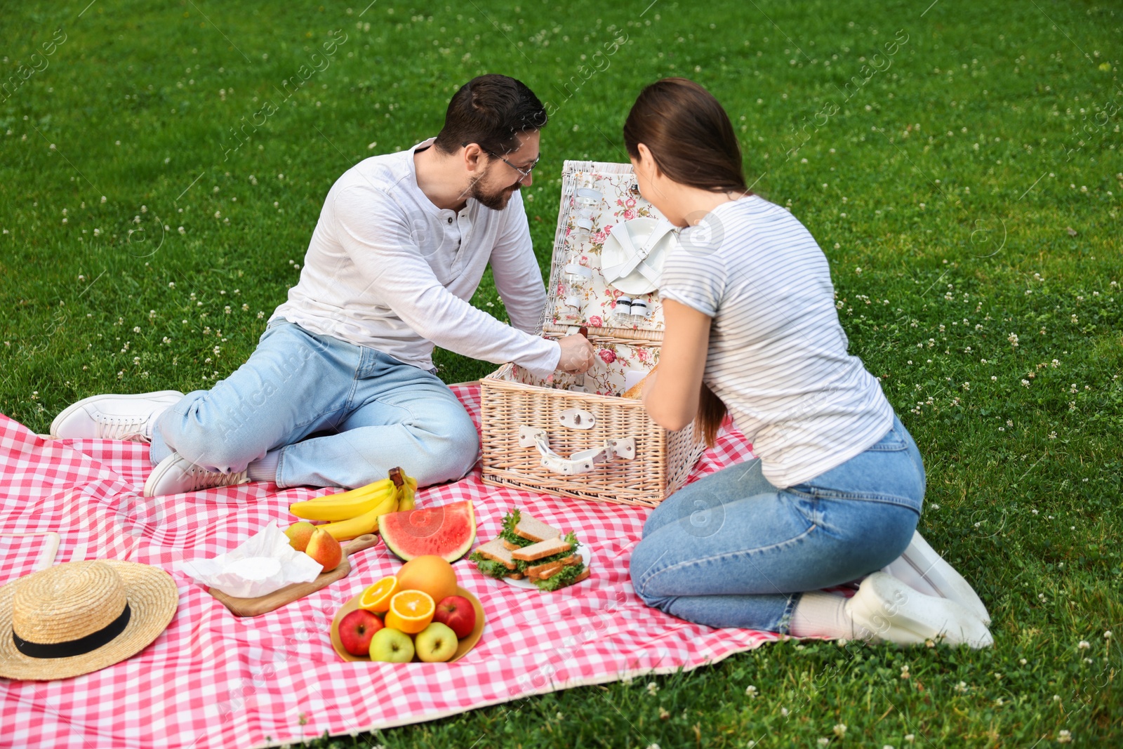 Photo of Happy couple having picnic on green grass outdoors