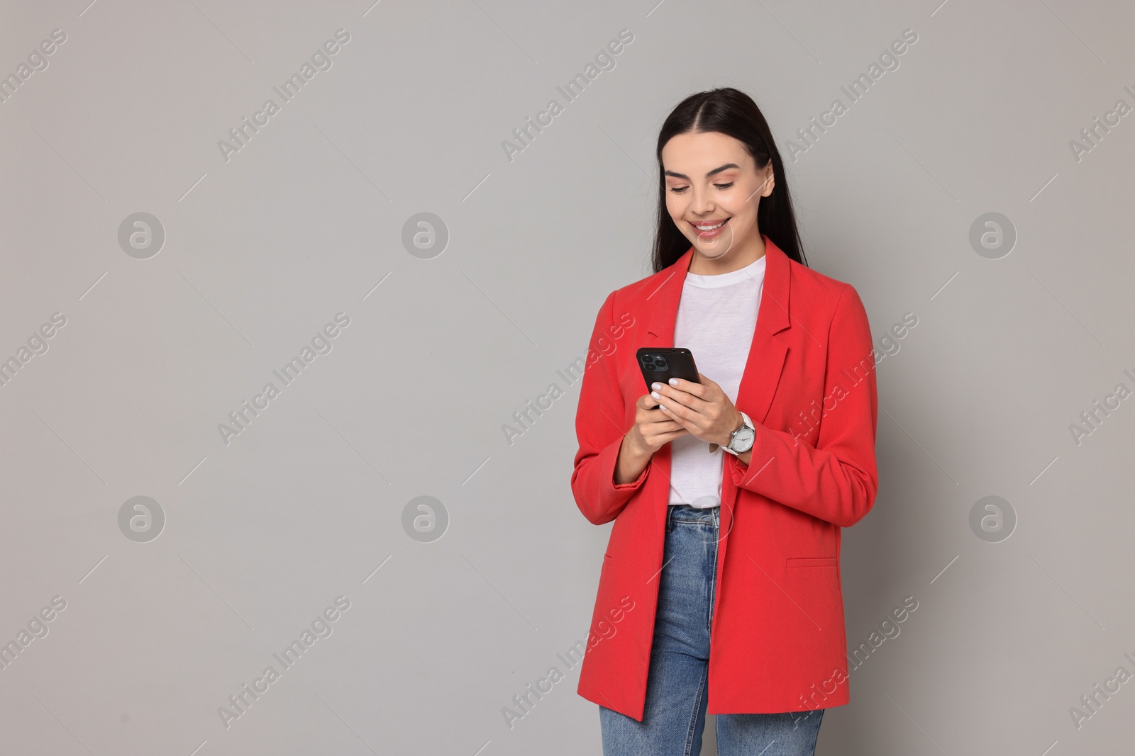 Photo of Beautiful woman in red jacket using smartphone on gray background, space for text