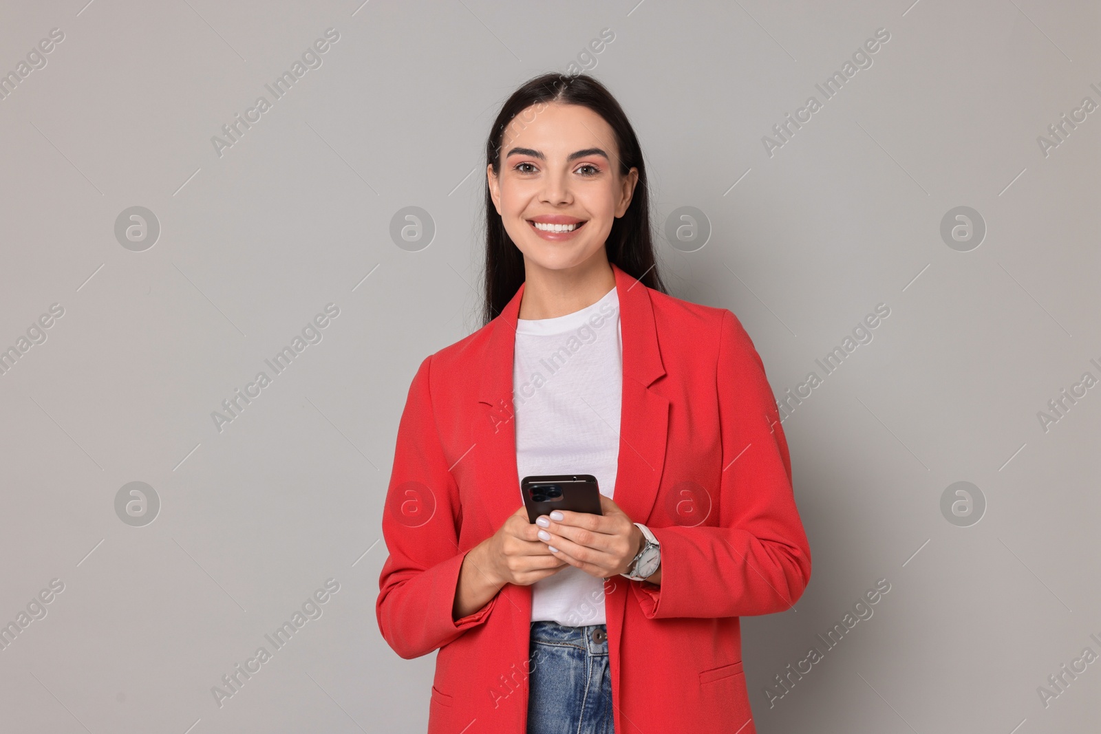 Photo of Beautiful woman in red jacket with smartphone on gray background