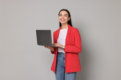 Photo of Beautiful woman in red jacket with laptop on gray background