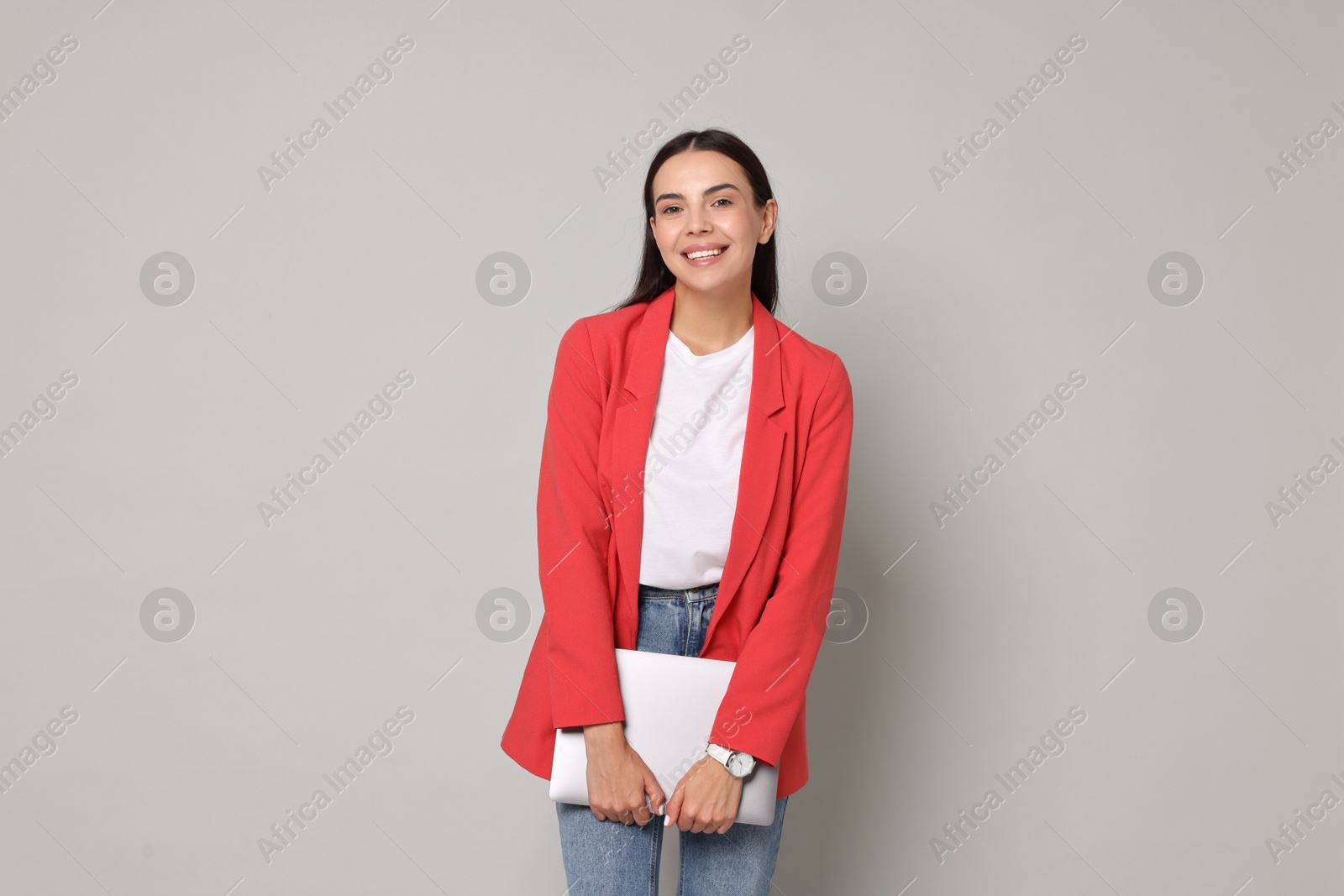 Photo of Beautiful woman in red jacket with laptop on gray background