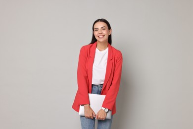 Beautiful woman in red jacket with laptop on gray background