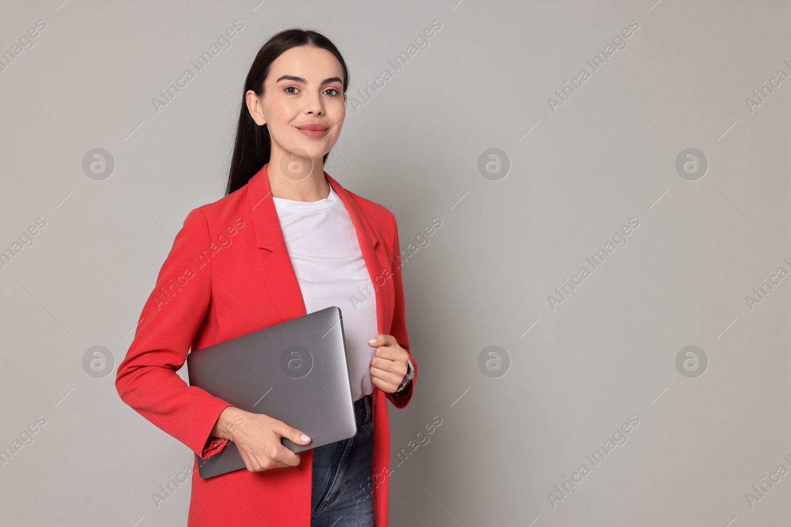 Photo of Beautiful woman in red jacket with laptop on gray background, space for text