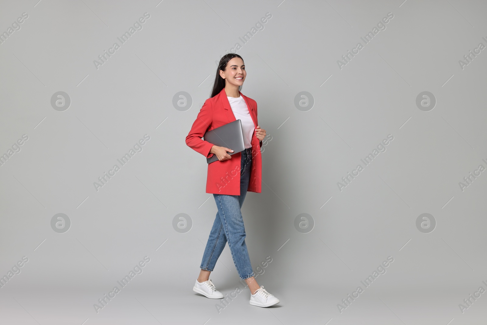 Photo of Beautiful woman in red jacket with laptop on gray background