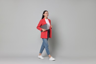 Beautiful woman in red jacket with laptop on gray background