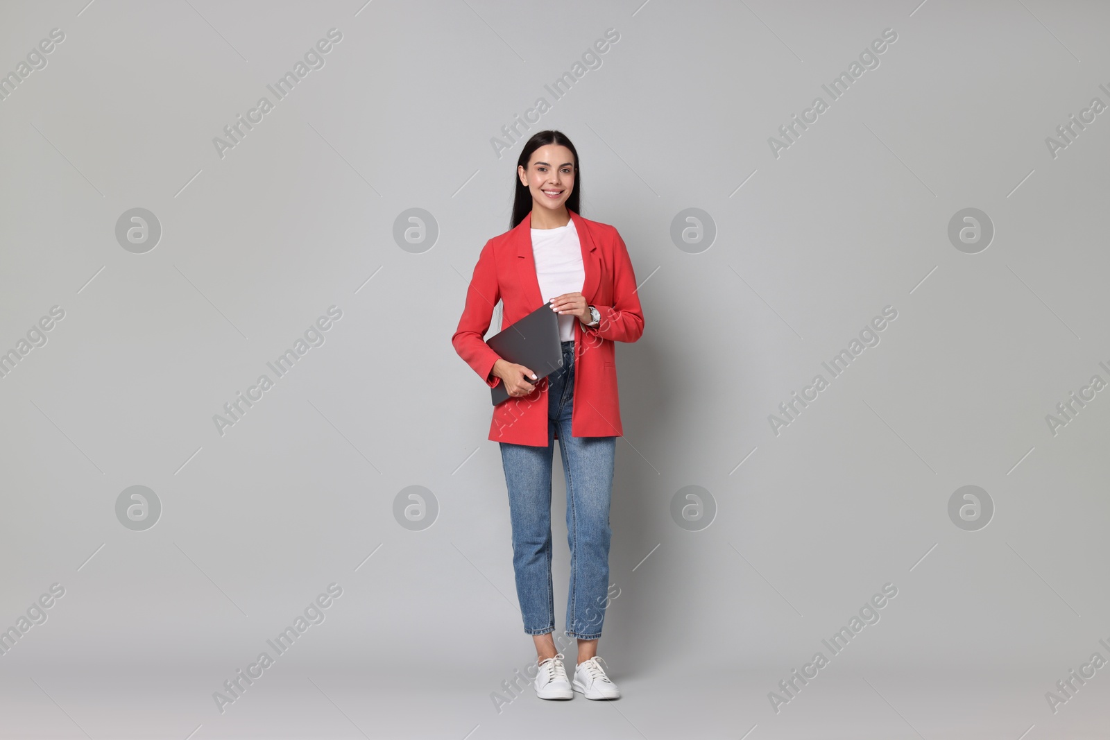 Photo of Beautiful woman in red jacket with laptop on gray background