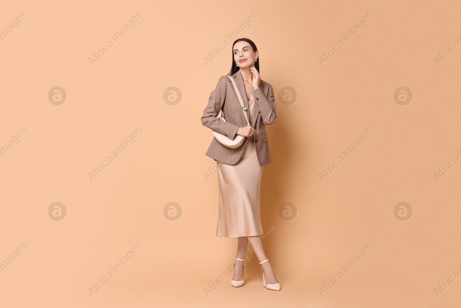 Photo of Beautiful woman in stylish jacket with bag on pale orange background