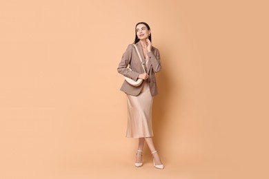 Photo of Beautiful woman in stylish jacket with bag on pale orange background