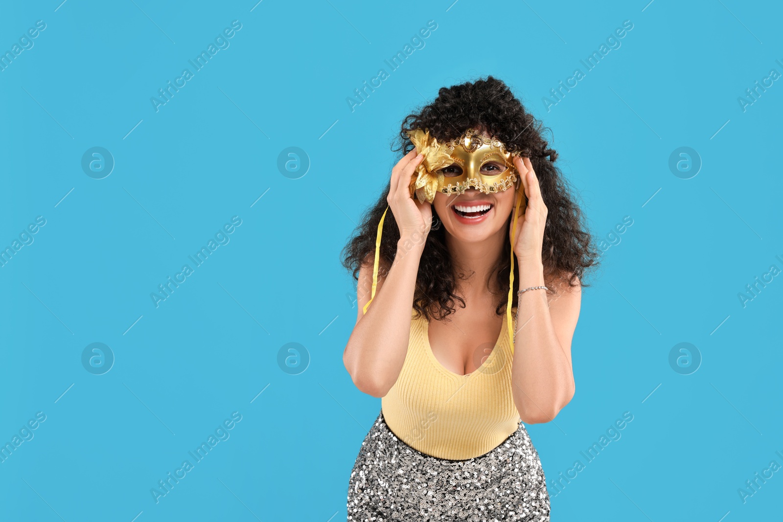 Photo of Happy young woman with carnival mask on light blue background, space for text