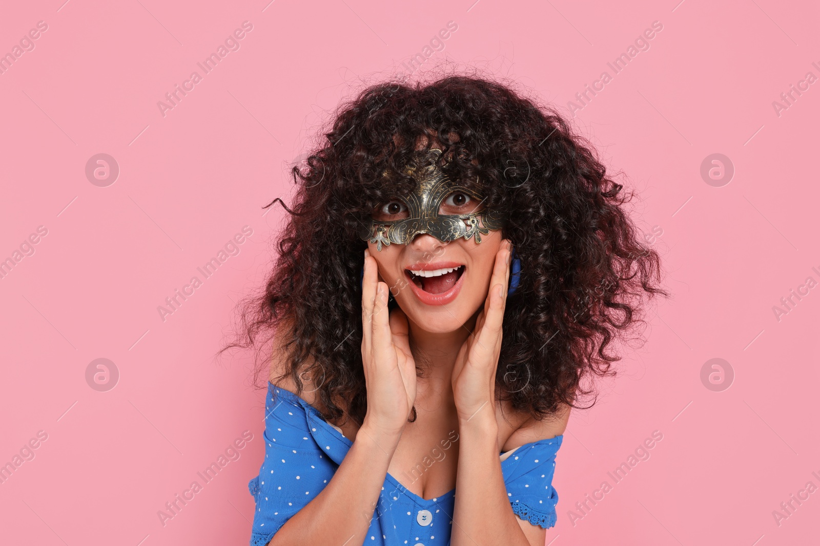 Photo of Emotional young woman wearing carnival mask on pink background