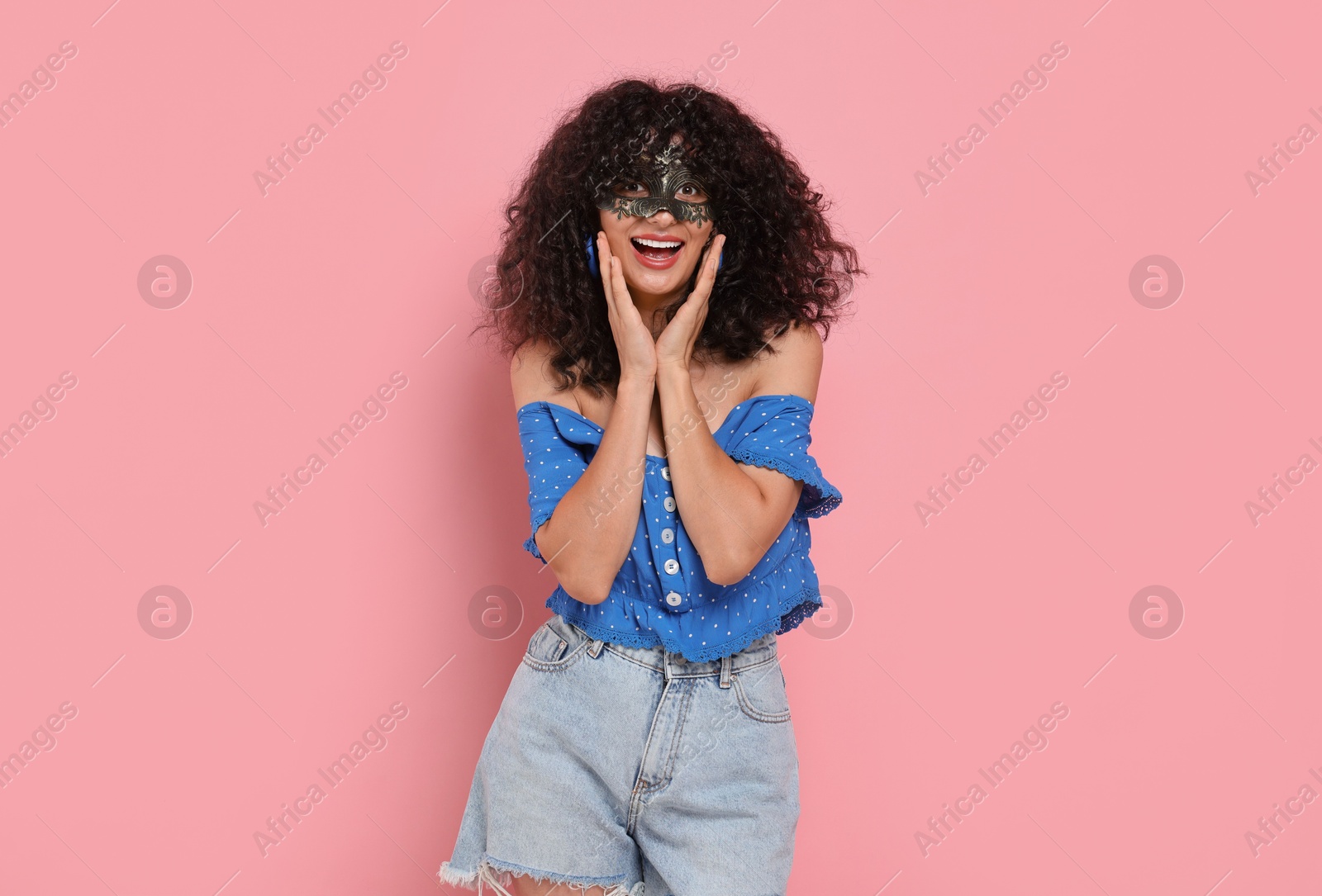 Photo of Happy young woman wearing carnival mask on pink background