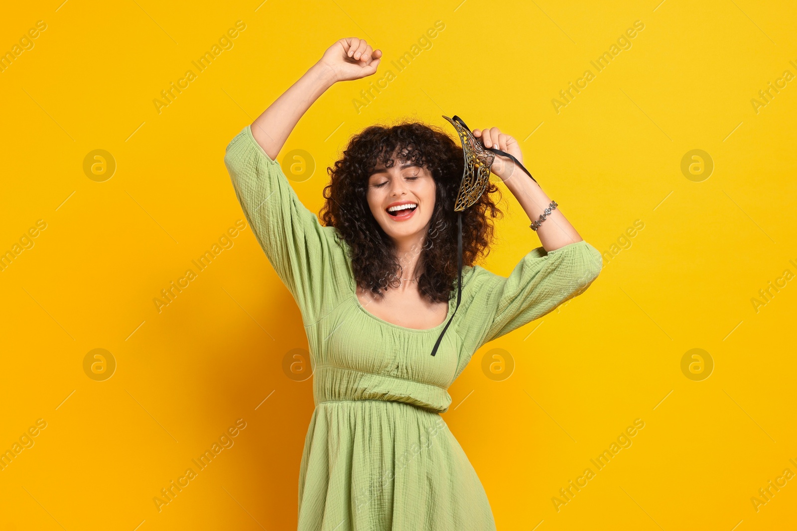 Photo of Smiling young woman with carnival mask on yellow background