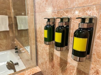 Bottles with body care products on tiled wall in hotel bathroom