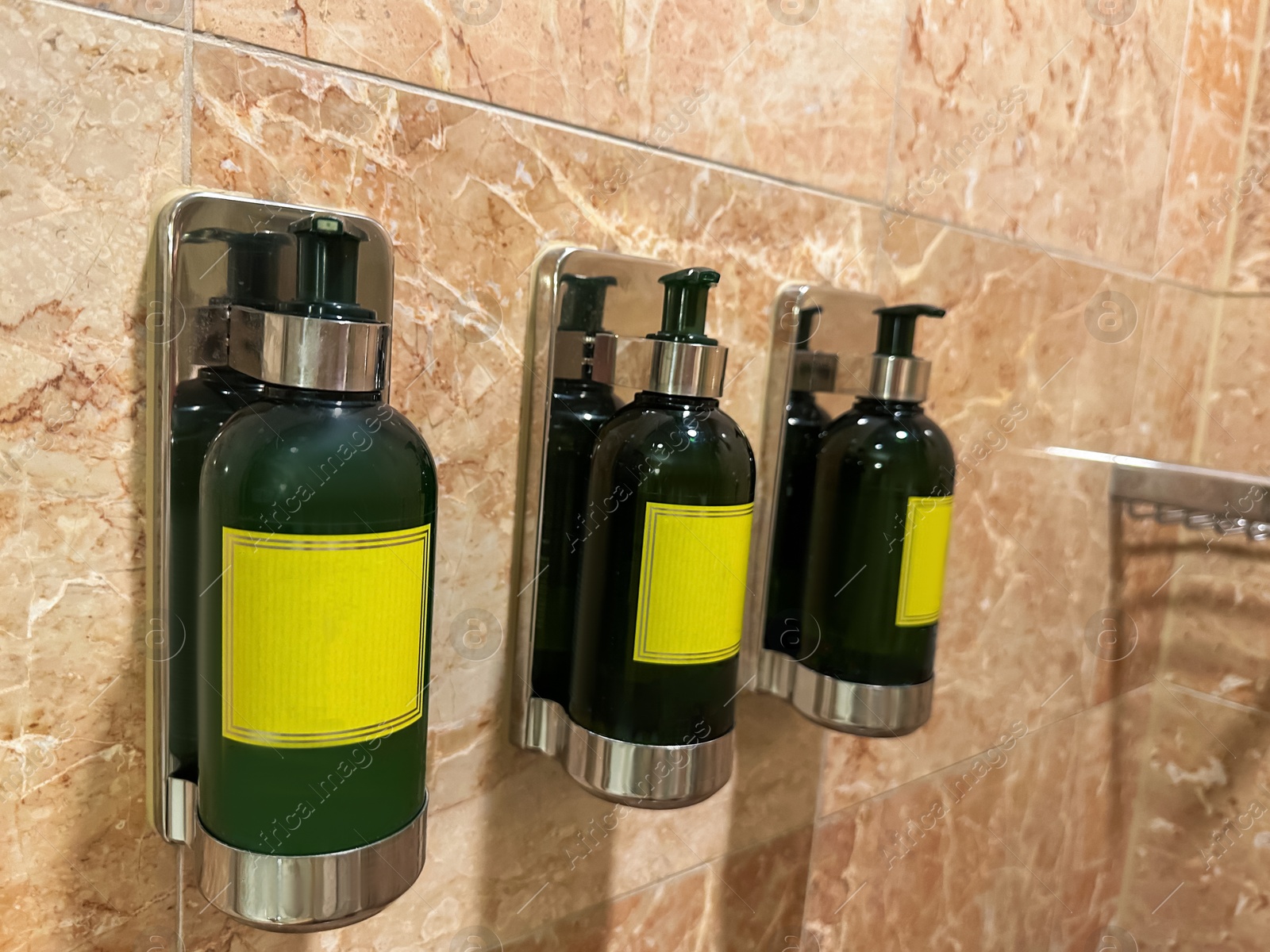 Photo of Bottles with body care products on tiled wall in hotel bathroom