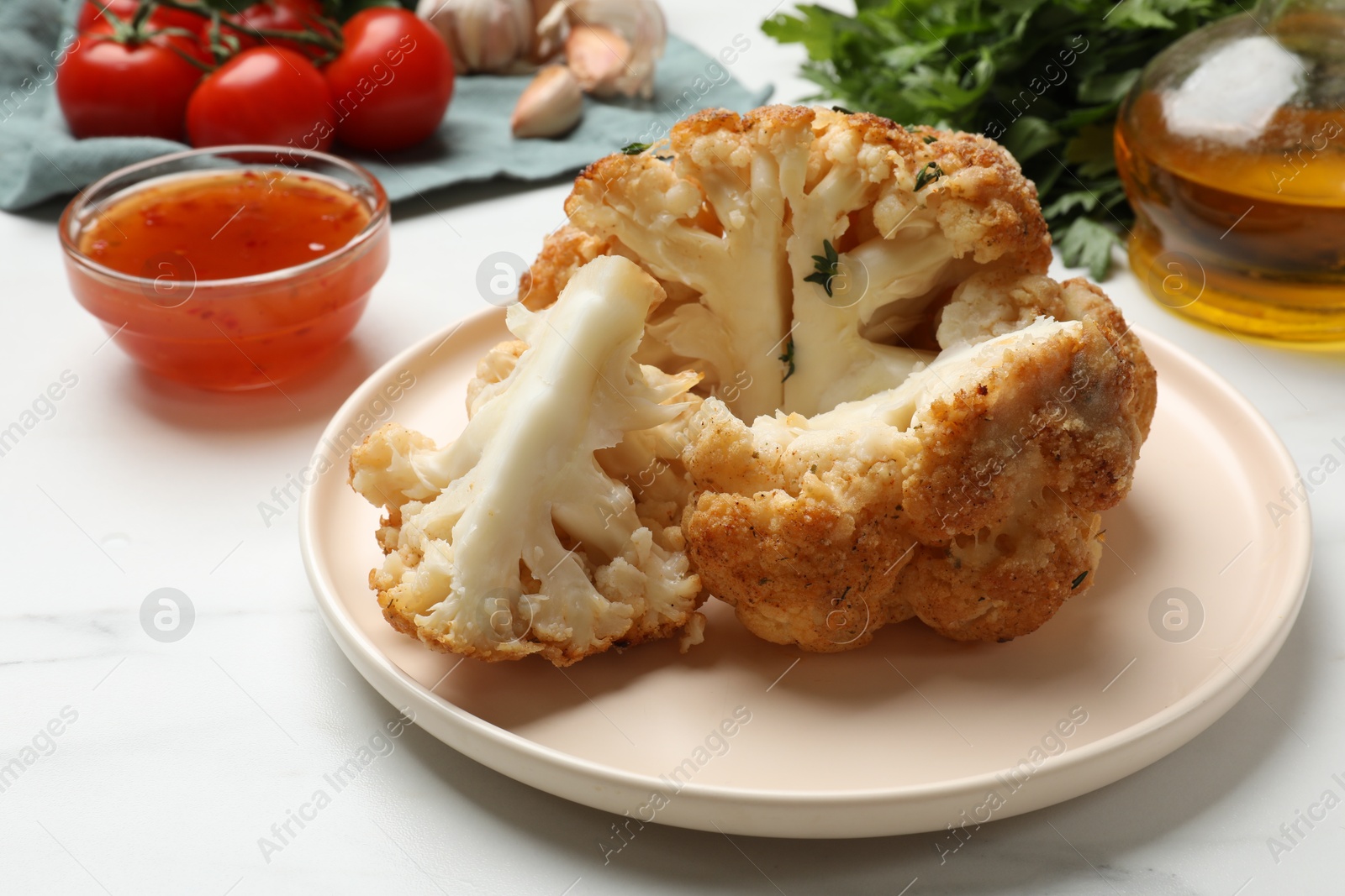 Photo of Delicious baked cauliflower and products on white table, closeup