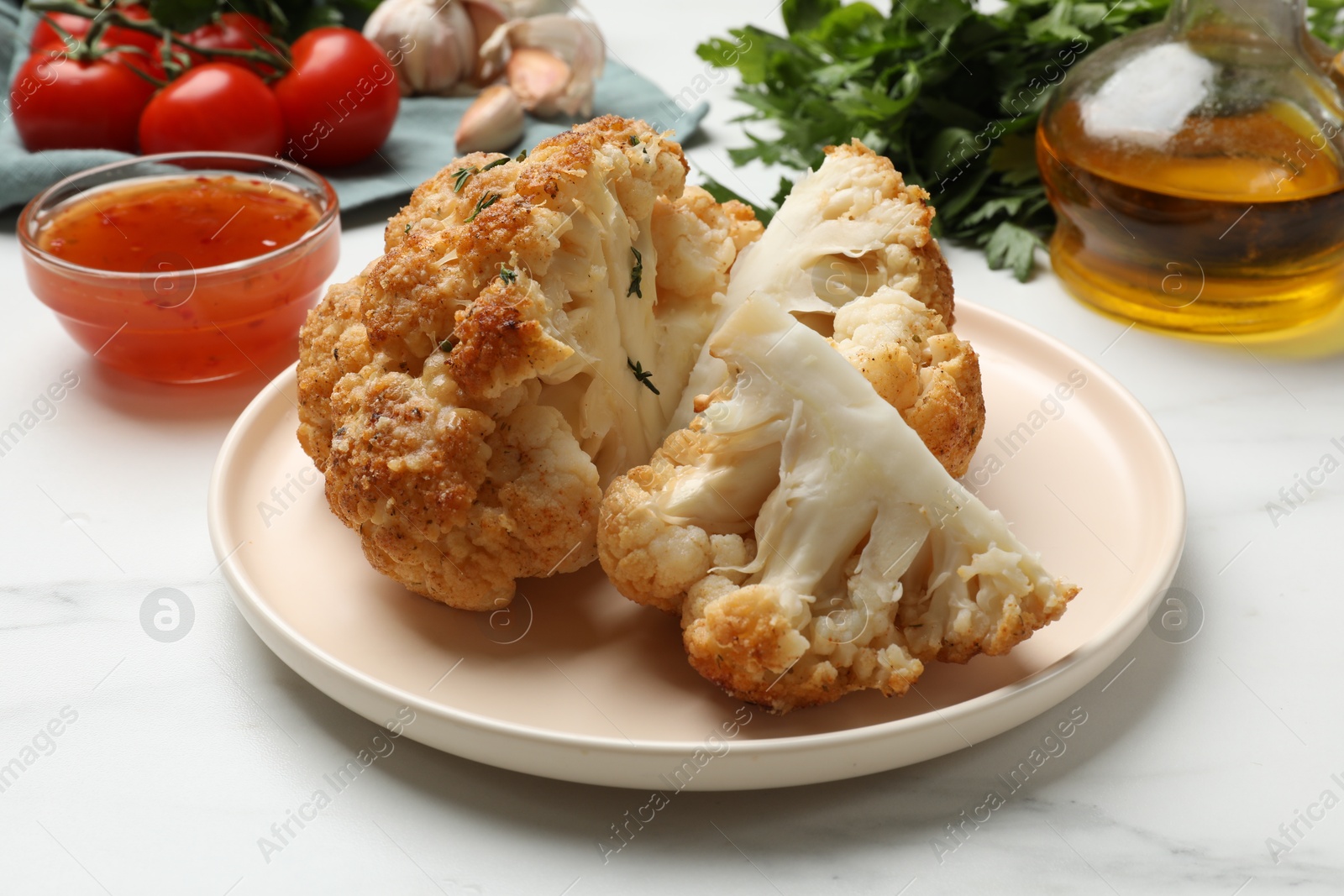 Photo of Delicious baked cauliflower and products on white table, closeup