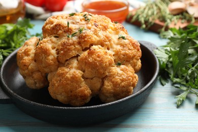 Photo of Delicious baked cauliflower in baking dish and products on light blue wooden table, closeup