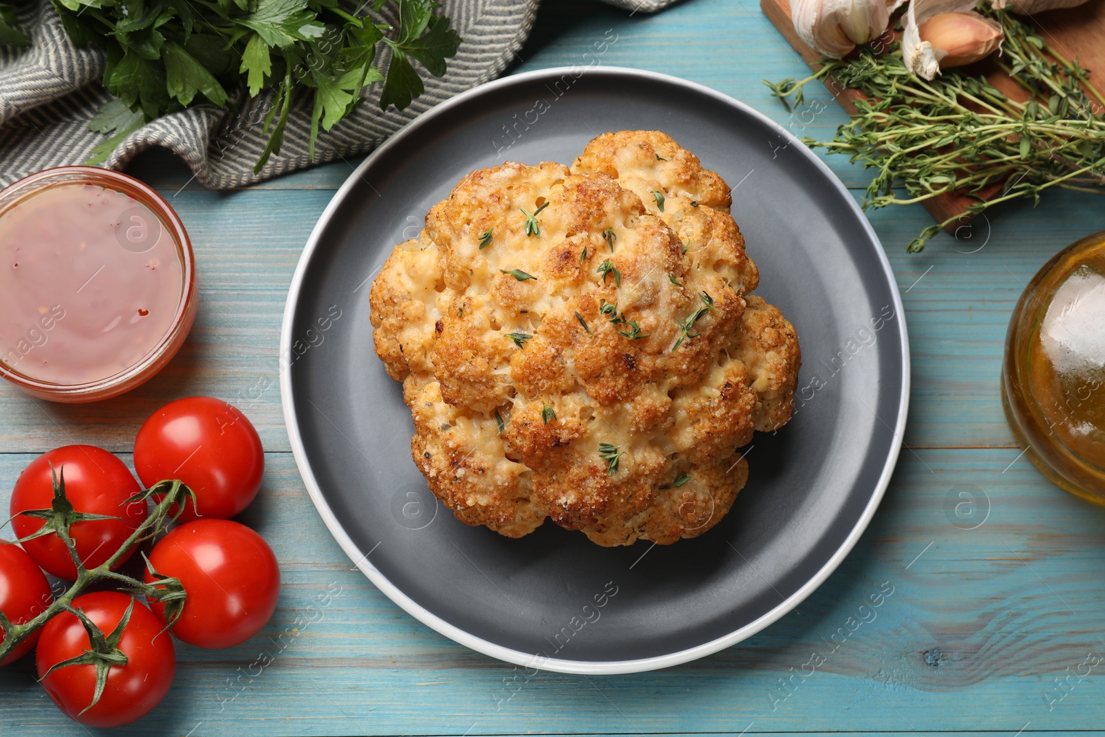 Photo of Delicious baked cauliflower and products on light blue wooden table, flat lay