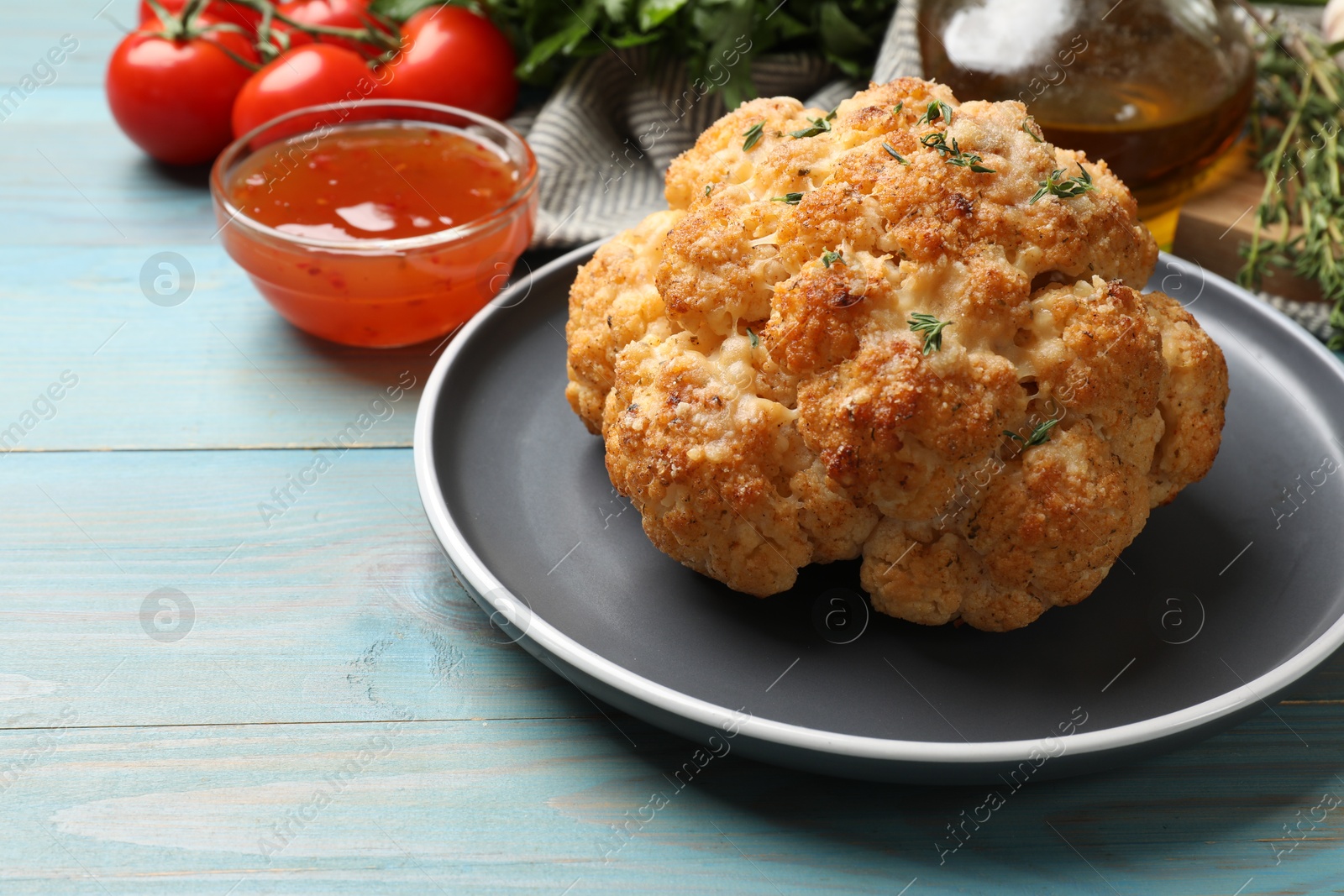 Photo of Delicious baked cauliflower and products on light blue wooden table, closeup