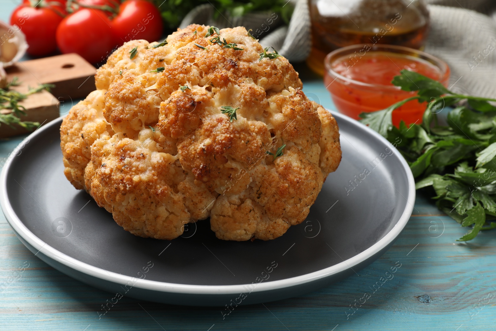 Photo of Delicious baked cauliflower and products on light blue wooden table, closeup