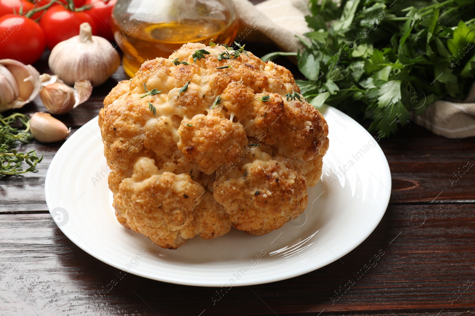 Photo of Delicious baked cauliflower and products on wooden table, closeup