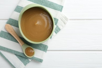 Photo of Delicious baby food in bowl on white wooden table, top view. Space for text