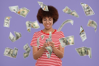 Happy woman using mobile phone under money rain on violet background