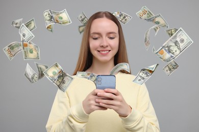 Happy woman using mobile phone on grey background. Money out of device flying around her