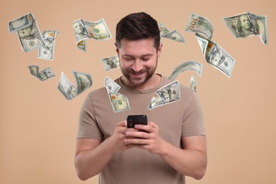 Happy man using mobile phone on dark beige background. Money out of device flying around him