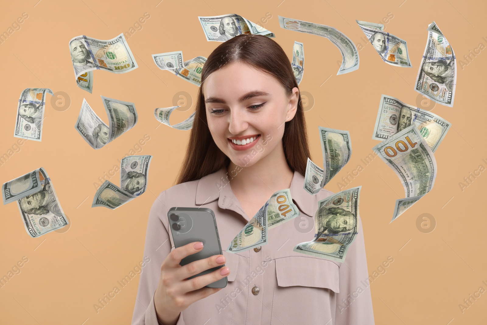 Image of Happy woman using mobile phone on dark beige background. Money out of device flying around her