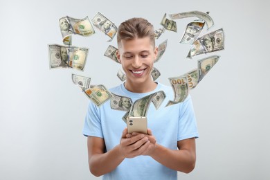 Happy man using mobile phone on light grey background. Money out of device flying around him