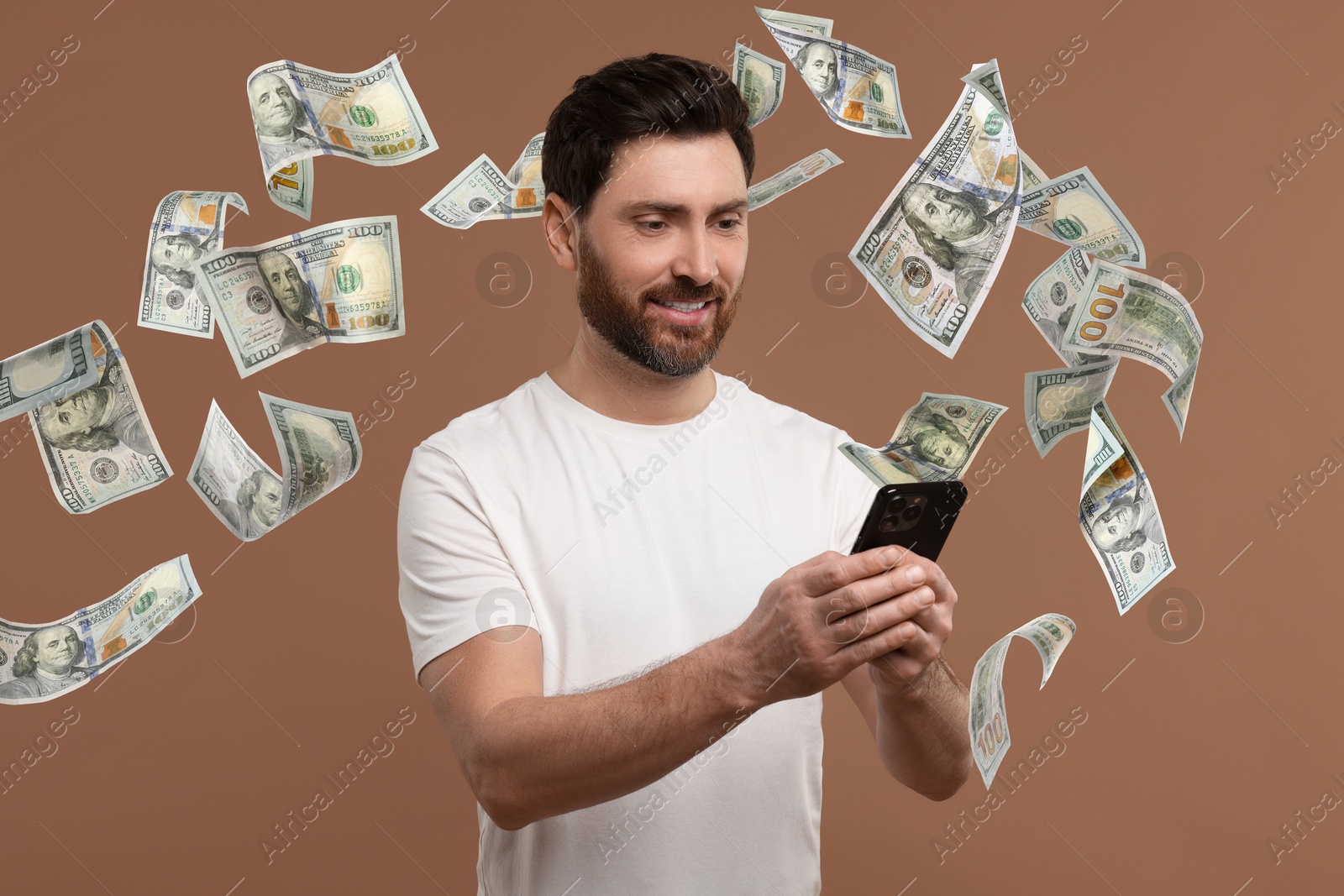 Image of Happy man using mobile phone on dark beige background. Money out of device flying around him