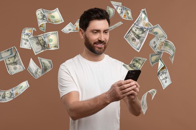 Happy man using mobile phone on dark beige background. Money out of device flying around him