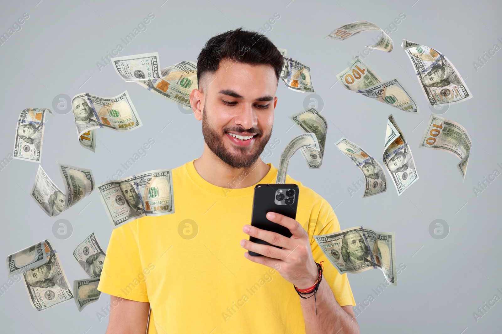 Image of Happy man using mobile phone on grey background. Money out of device flying around him