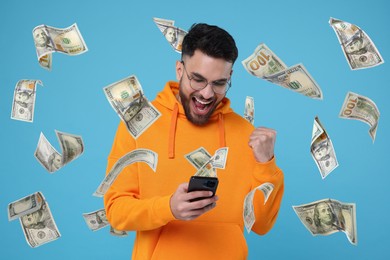 Happy man using mobile phone under money rain on light blue background