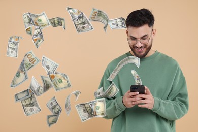 Image of Happy man using mobile phone on beige background. Money out of device flying around him