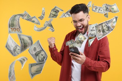 Happy man using mobile phone on orange background. Money out of device flying around him