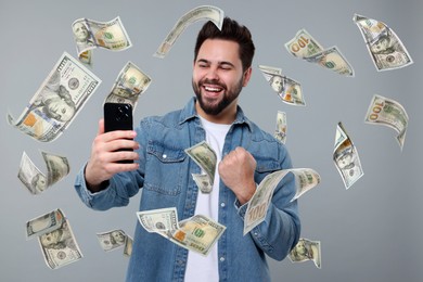 Happy man using mobile phone under money rain on grey background