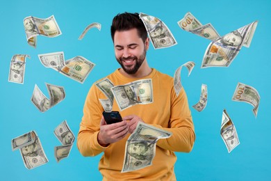 Happy man using mobile phone under money rain on light blue background