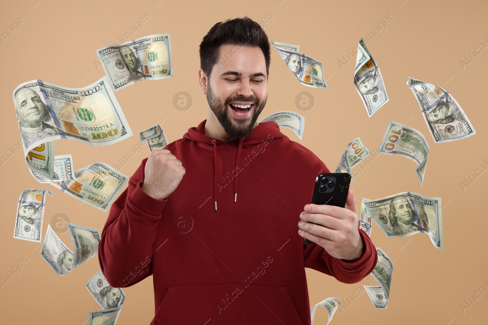 Image of Happy man using mobile phone on dark beige background. Money out of device flying around him