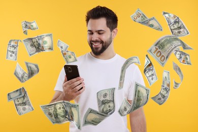 Image of Happy man using mobile phone on orange background. Money out of device flying around him