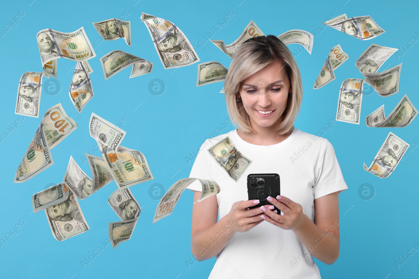 Image of Happy woman using mobile phone on light blue background. Money out of device flying around her