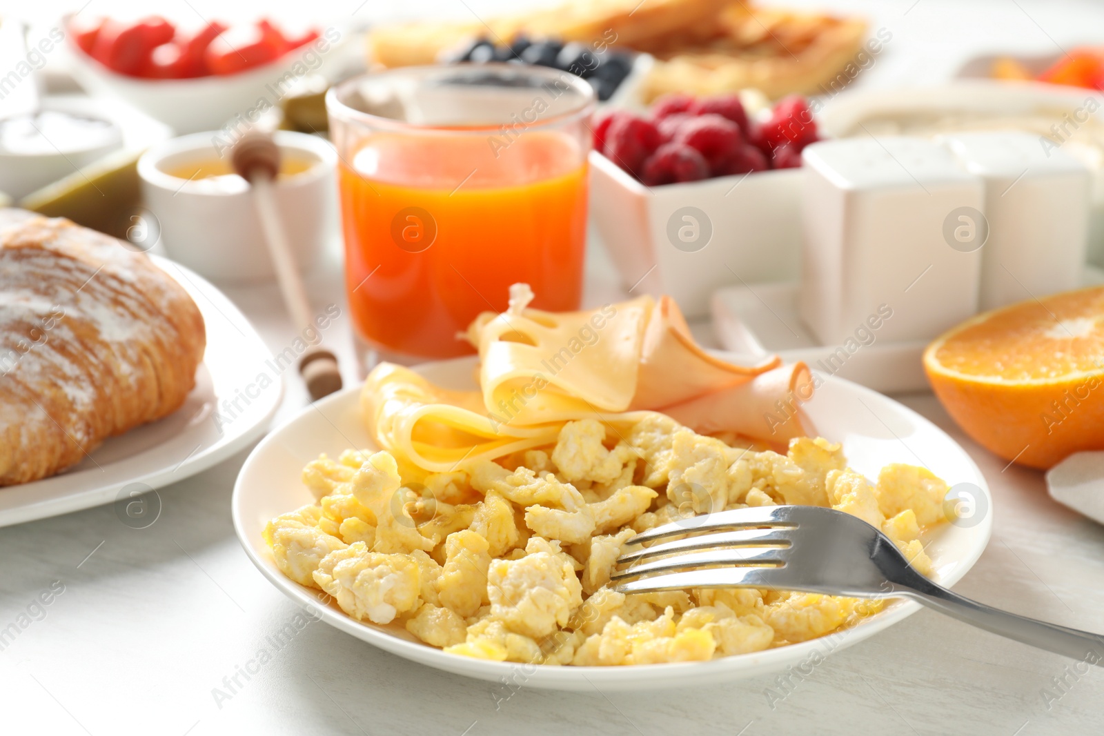 Photo of Tasty breakfast. Scrambled eggs, ham, cheese and other food served on light wooden table, closeup